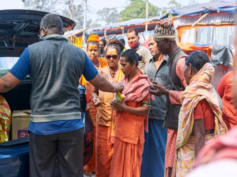 Babughat, Kolkata, 01/09/2021: Member of a welfare association giving free food (fruits, breads, milk, biscuits etc.) to the pilgrims coming to the transit camp for Gangasagar Mela 2021. Camps have been setup on ground as resting place for pilgrims and sadhus going to the mela to be held on the day of Makar Sankranti.